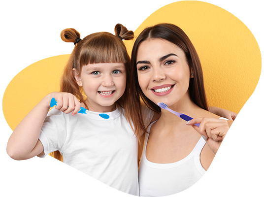 A woman and young girl smiling and holding toothbrushes